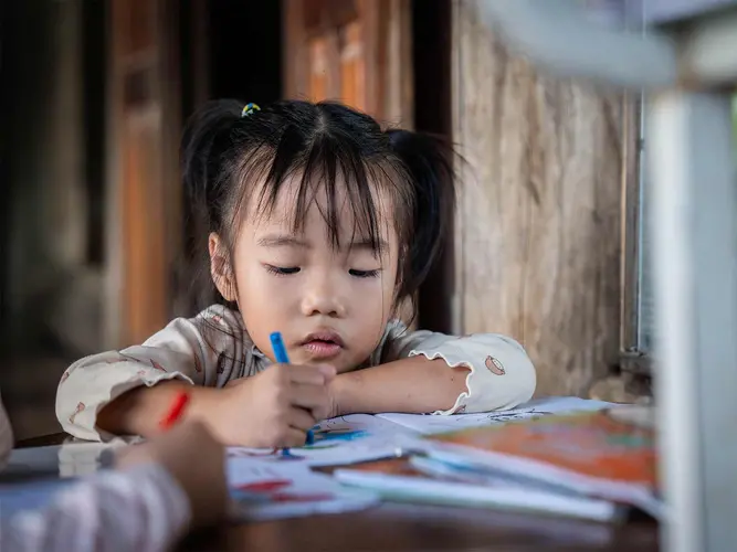 A little girl colors in her coloring books on a table.