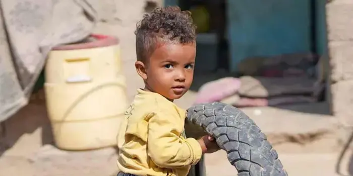 A young child with curly hair stands outside holding a bike tire.