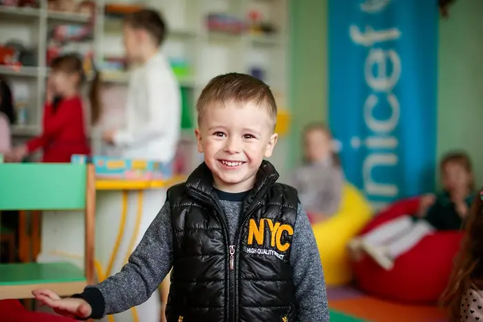 A boy in a classroom wears a jacket that says 'NYC' on the left side chest