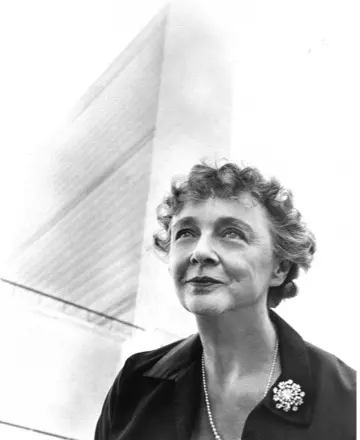 Black and white profile photo of Helenka Pantaleoni, a woman with curly short hair in a suit and broach. The United Nations Secretariat Building looms tall in background.