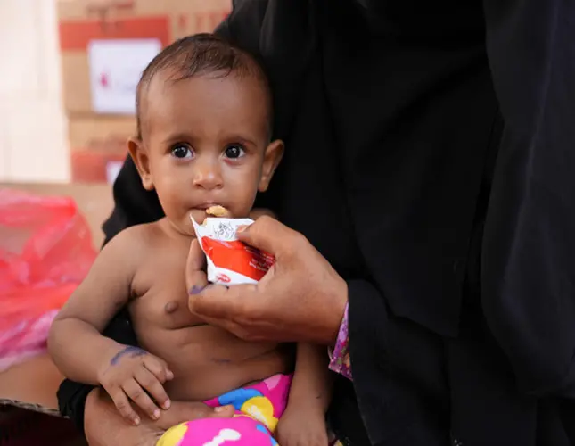 An infant in a mother’s arms eats from a sachet of ready-to-use-therapeutic food.