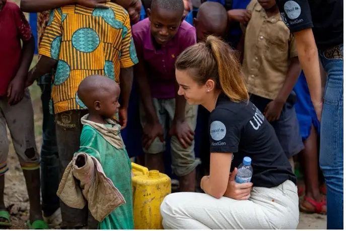 A young child looks into the face of a kneeling woman wearing a UNICEF t-shirt. Behind them is a crowd of chidlren and UNICEF workers.