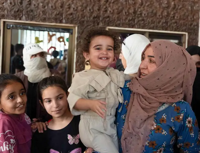 A mother holds a smiling child at a shelter for displaced families in Syria.