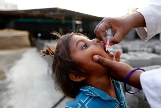 A woman gently squeezes a girl’s mouth open while holding a medicine dropper over her mouth.