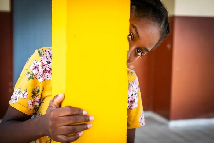 A young girl in Gabon peeks out from behind a pillar inside a child protection service center supported by UNICEF. 