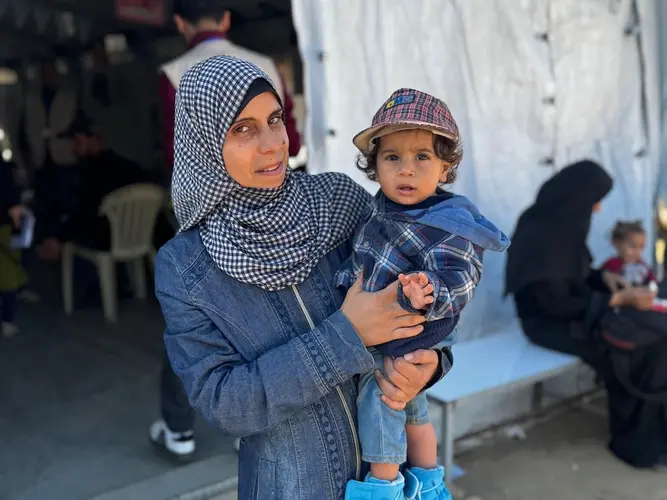 A mother holds her 1-year-old son outside a UNICEF-supported nutrition point in southern Gaza.