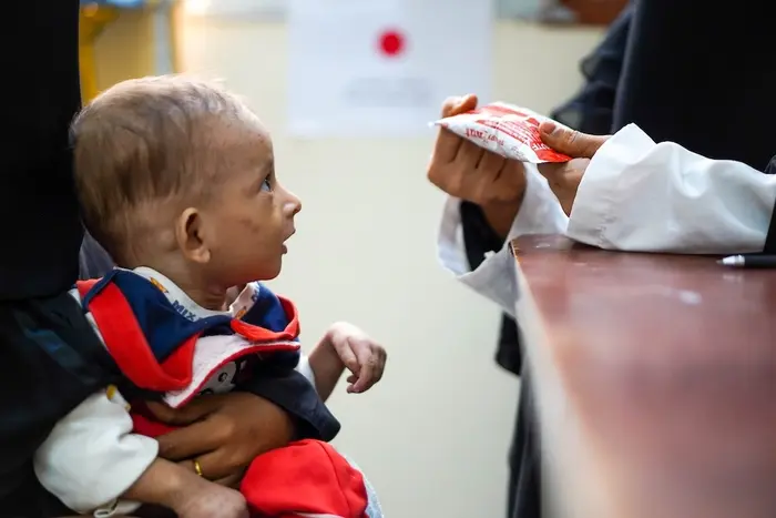 A caregiver presents a packet of RUTF to a child with severe acute malnutrition in Yemen. 