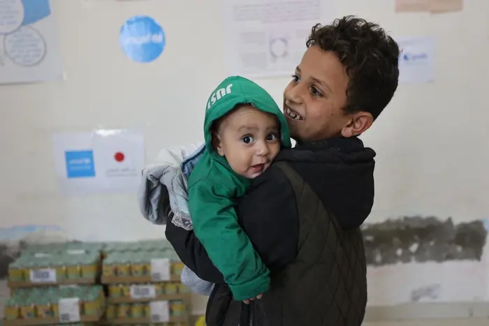 A boy holds his baby brother in a UNICEF ready-to-use complementary food distribution site in Gaza City. 