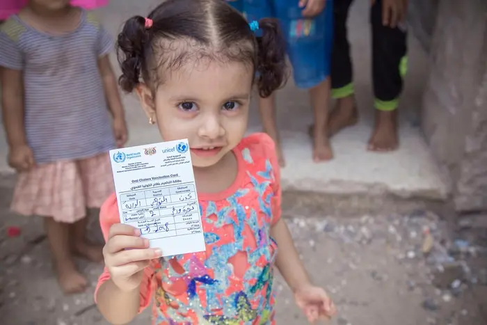 In Aden, Yemen, a young girl holds up her vaccination card.