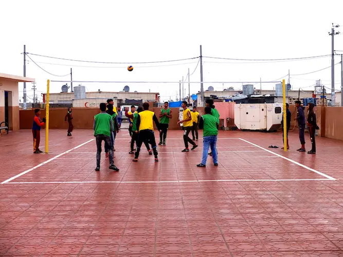 Boys play volleyball outside a series of offices for computer classes and women's vocational training, in Debaga camp in Iraq.