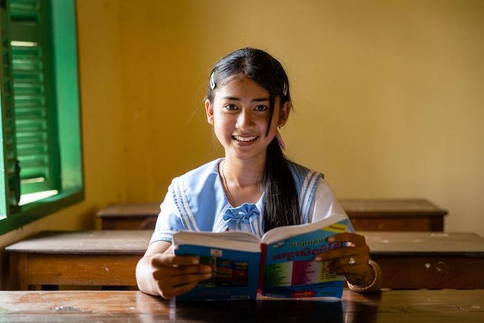 Ninth grade girl holding a book and smiling in her school