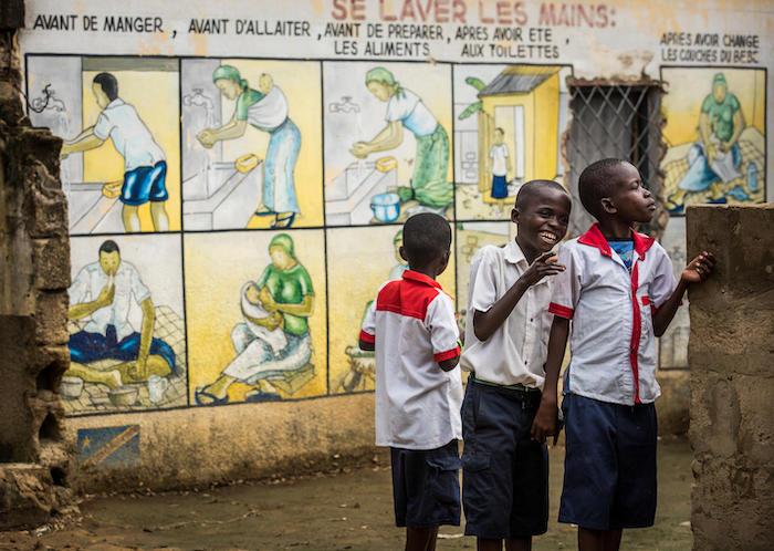 Students stand beside a mural illustrating the importance of handwashing in Kinshasa, Democratic Republic of the Congo. 