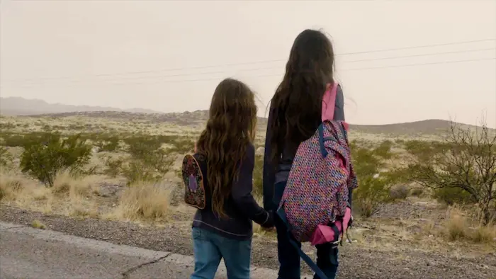 Two young girls with backpacks, child migrants from Guatemala, walk side by side through scrubby terrain. Two young girls with backpacks, child migrants from Guatemala, walk side by side through scrubby terrain.