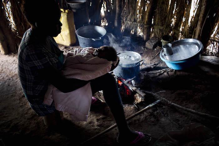 Esther, 18, holds her baby as she prepares food inside her home in Yambio, South Sudan.