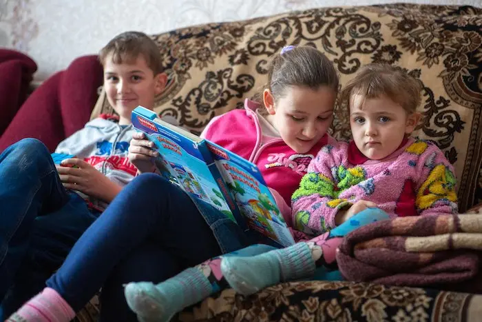 Sergiy,11, Tanya, 10 and Anna, 4 reading a book at their home in Pokrovsk. The family with five children has been suffering hardship, since the conflict began. © UNICEF/UN0300591/Filippov