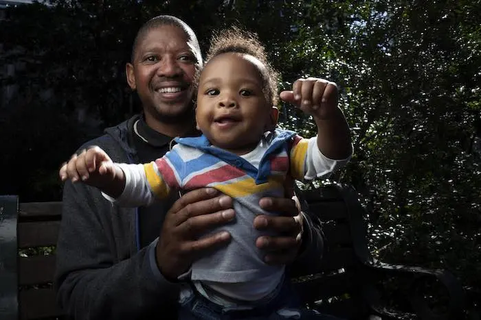 Bongani Ngqame, 44, holds his son, Khuma, 8 months, during a portrait shoot at a park near his office at the Department of Health in Cape Town, South Africa on 9 May 2019. Sunlight filters through the trees as the bright-eyed baby coos and smiles. "I took