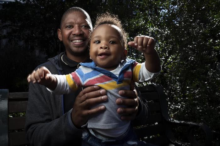 Bongani Ngqame, 44, holds his son, Khuma, 8 months, during a portrait shoot at a park near his office at the Department of Health in Cape Town, South Africa on 9 May 2019. Sunlight filters through the trees as the bright-eyed baby coos and smiles. "I took