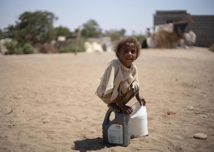 A child from Yemen's Al-Meshqafah camp plays while carrying water home from UNICEF-supported tanks in 2019.