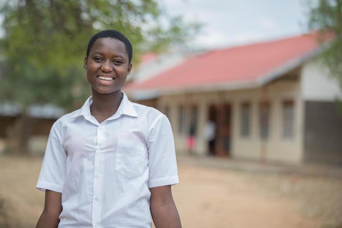 Teenage girl smiles at camera in front of a student center in Uganda