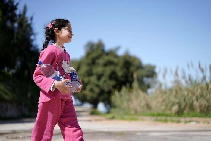 Syrine, 10, heads for home in Wadi El Jamous, Lebanon, with two newly-refilled bottles of water.