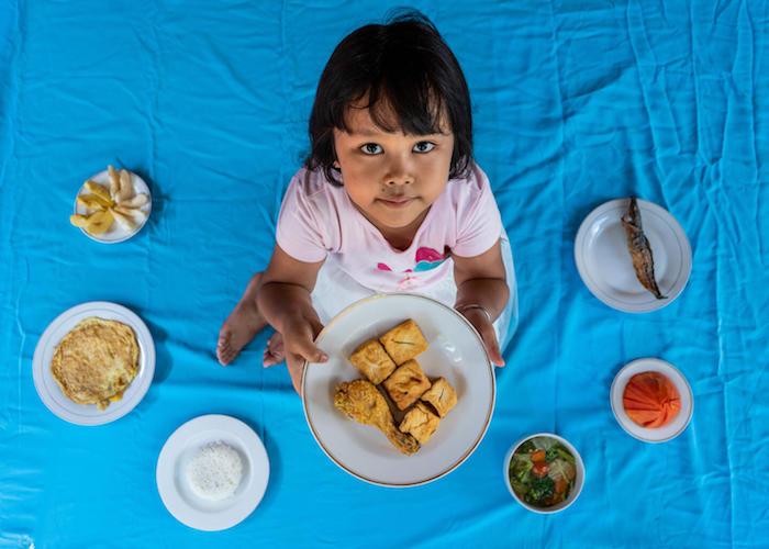 Helga, 5, holds a plate of fried chicken and tofu at her home in Pandes Village, Klaten, Central Java Province, Indonesia on September 7, 2021. 