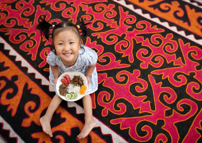 Nurayim, 3, holds a plate of nutritious food at her home in Kurshab village, Uzgen district, Osh Oblast, Kyrgyzstan.