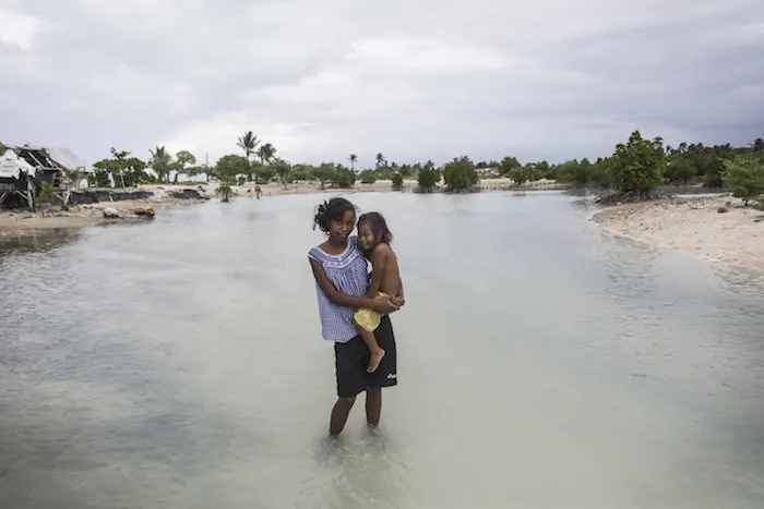 Taronga, 16, holds her two-year-old sister Teaborenga while standing in a flooded area in the village of Eita, South Tarawa, Kiribati, Thursday 28 January 2016. UNICEF, climate change, flooding, Kiribati