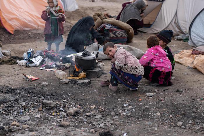 Suraya, 8, and her sisters huddle over an open fire, trying to stay warm, outside their tent at the IDP camp where they live in Herat Province, Afghanistan.