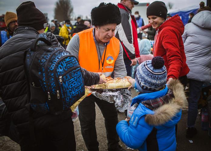 A volunteer offers warm bread to Nichita, 7, in Isaccea, Romania. He and his mother crossed the Danube by ferry from Ukraine on March 4, 2022.