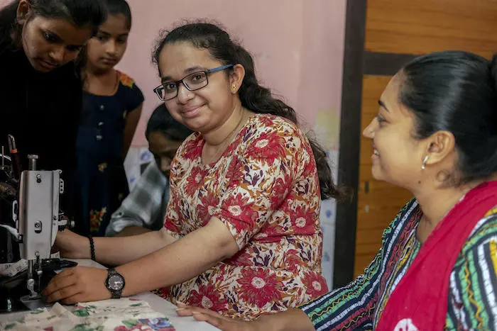 Teenage girl smiles next to the sewing machine she is using during a vocational training program Teenage girl smiles next to the sewing machine she is using during a vocational training program
