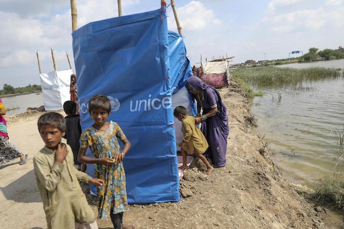 A mother and child duck under a UNICEF blue tarp where they are sheltering roadside after fleeing their flood-hit home in Mirpur Khas District, Sindh Province, Pakistan.