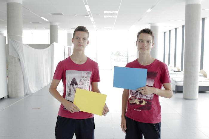 Two 15-year-old twin brothers from Odessa, volunteering in a Blue Dot center in Brasov, Romania, hold up yellow and blue pieces of paper