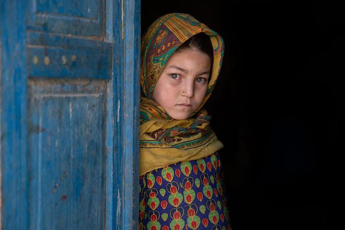 Nine-year-old Asna stands by the door at her home in Afghanistan.