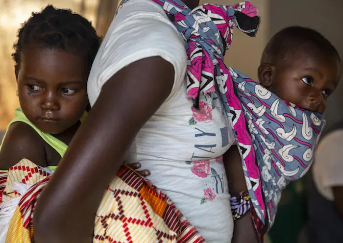 In March 2020, a mother carries her feverish children, 3-year-old Eliza and 6-month-old Domiqo, to a UNICEF health center in the Ndjenja resettlement camp in Mozambique. 