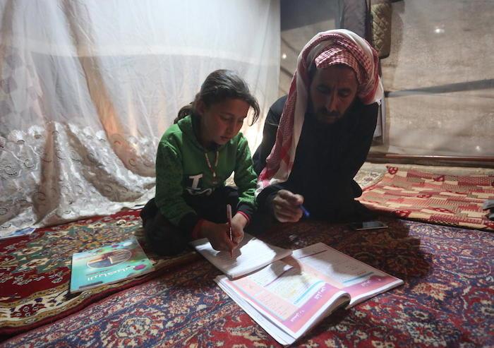 9-year-old Maria and her father follow a pre-recorded lesson on her father’s smartphone in a tent at the Kili IDP camp in rural Idlib, Syria.