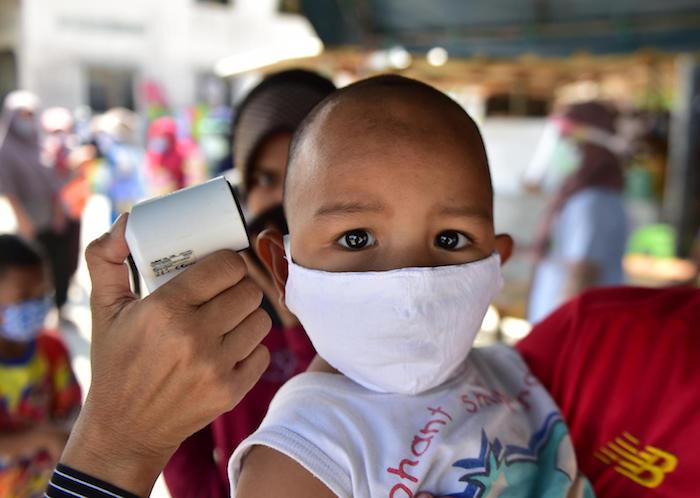 A young child has his temperature checked as people receive food support at a program organized by the Southern Peace Media Club in Thailand's southern province of Narathiwat on April 17, 2020.