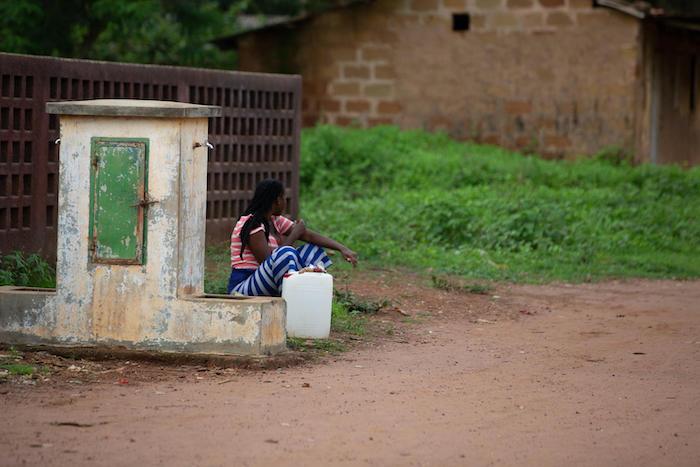 A woman in Koba, Kindia, Guinea, waits to fill her jug with water from a community access point.