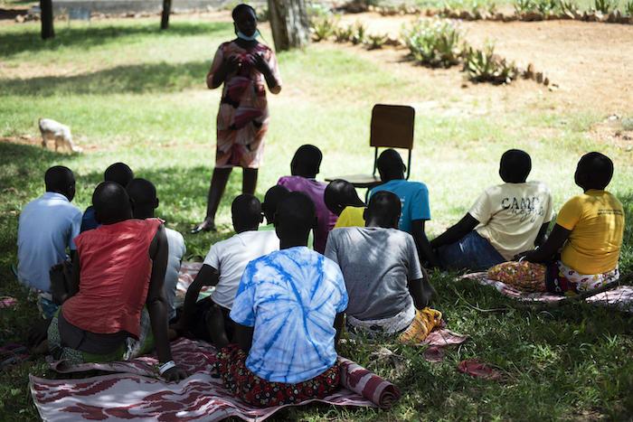 Adolescent girls sit in a cirle in front of an instructor in a park in Uganda 