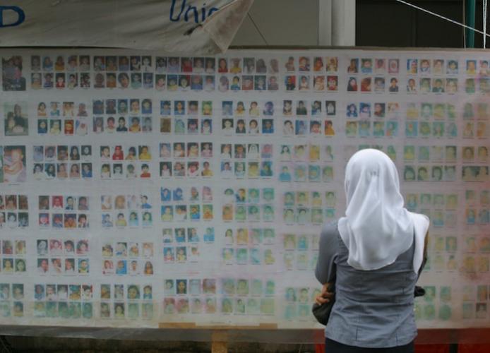 In Indonesia in 2005, a woman searches for her missing child on a board showing photos of children who have become separated from their families. 