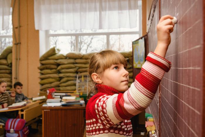 Fourth grader Angelina, 10, writes on a blackboard at School No. 2, Marinka, Ukraine, January 2017. Sandbags reinforce the windows to prevent them from shattering during frequent shelling. 