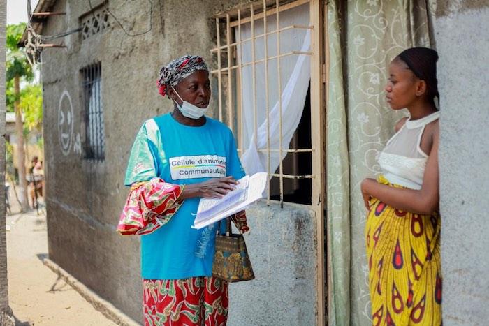 A member of a Community Action Cell speaks to a woman outside her home in Kinshasa to answer questions like "How safe is theCOVID-19 vaccine?"