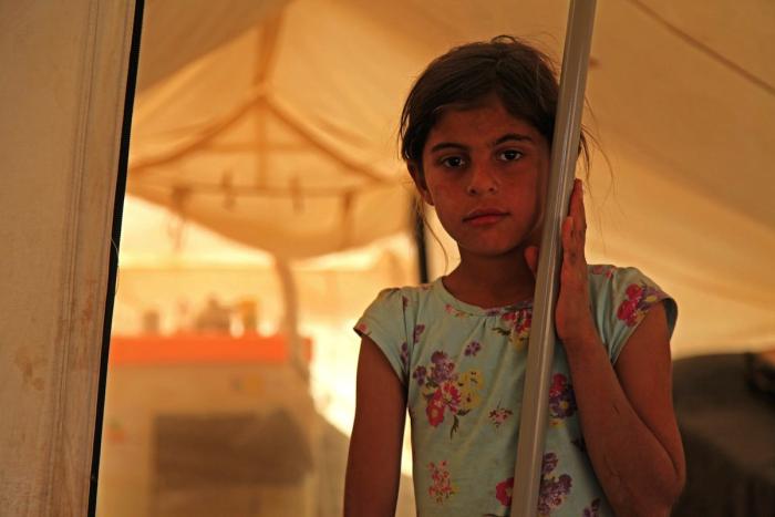 On 29 June 2014 in Iraq, 9-year-old Rasha Saleh, whose family has been displaced from the Kokjeli area in the conflict-affected city of Mosul, stands by a pole at the entrance to a tent in the Khazar transit camp in the northern-eastern city of Erbil.