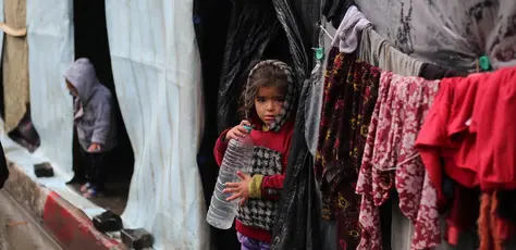 A little girl stands in front of her family's tent , holding an empty water bottle in the city of Rafah, southern Gaza Strip.