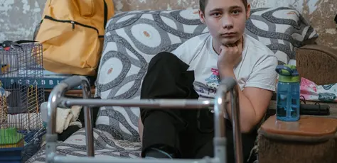 In Nikopol, Kharkiv oblast, eastern Ukraine, Nazar, 13, sits in his family's living room, his walker nearby. His legs and feet were injured by an explosive remnant of war. 