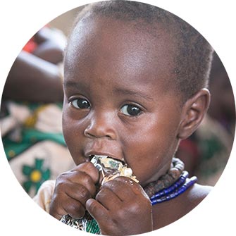 A child looks at the camera while eating something with both hands at their mouth